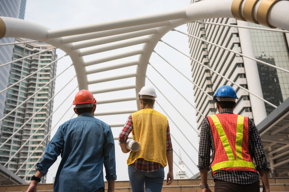Three construction workers staring at a bridge behind a skyline