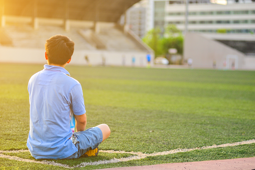 Lone boy sitting in a football field