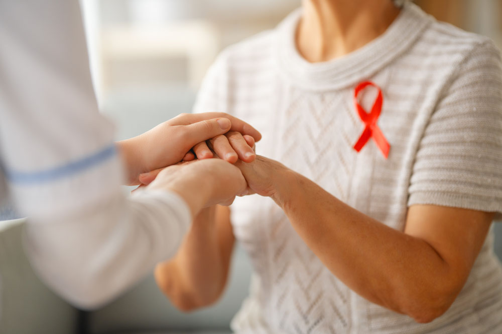 Nurse wearing a red ribbon for HIV/AIDS awareness holding a patient's hand